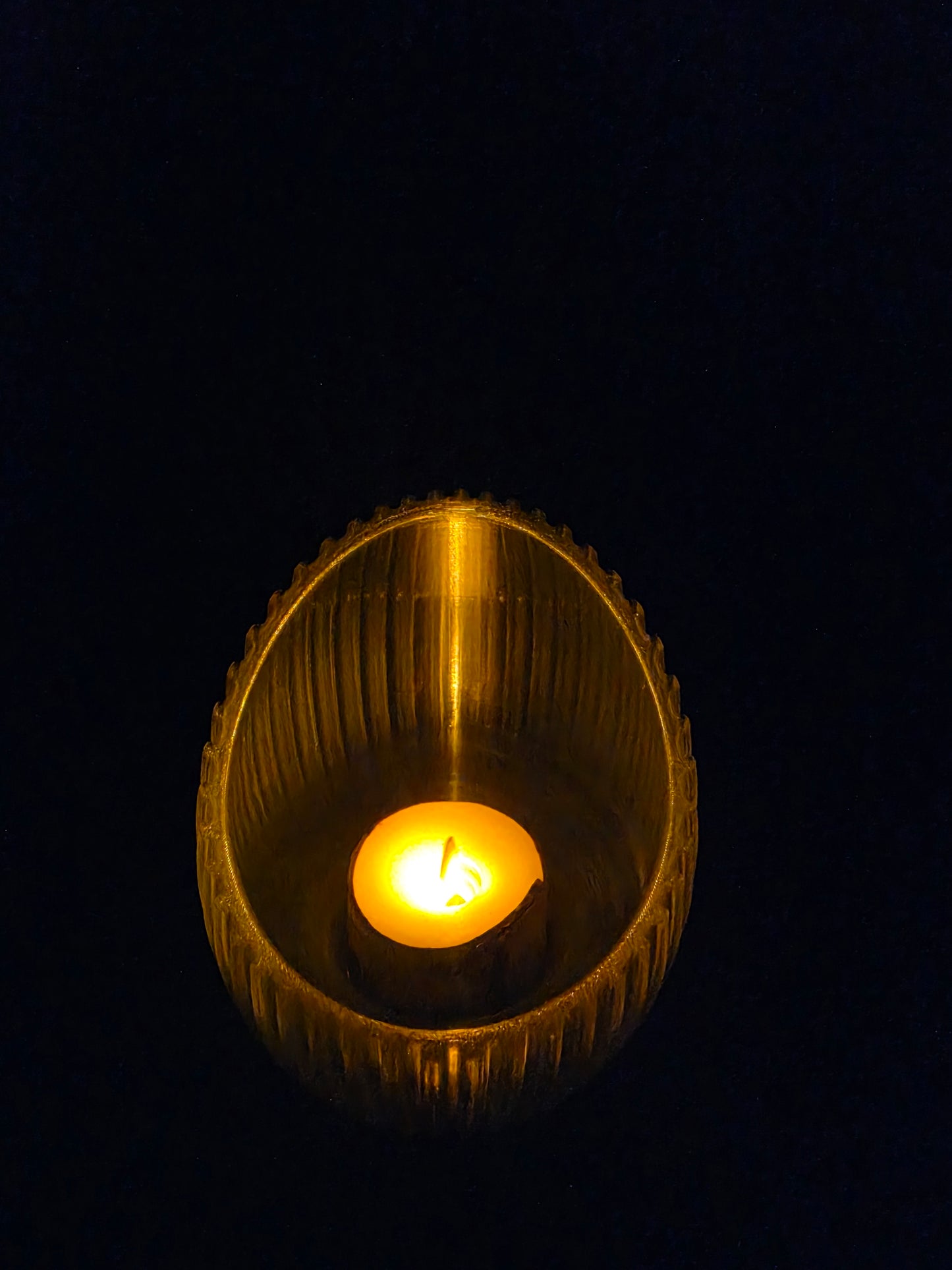 Close-up of a lit candle inside a textured gold holder against a black background