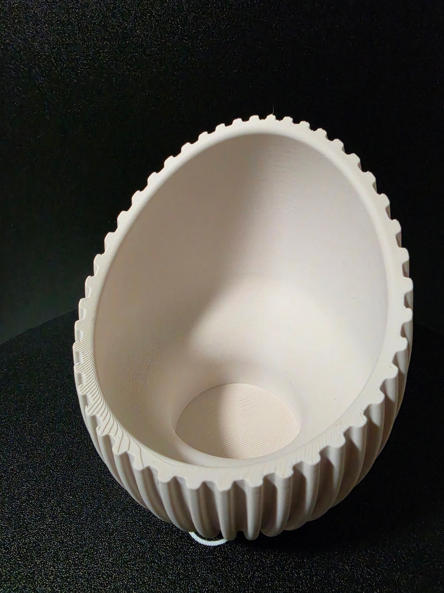 A white plastic or resin bowl-shaped component with a fluted outer edge, photographed from above on a black textured background.
