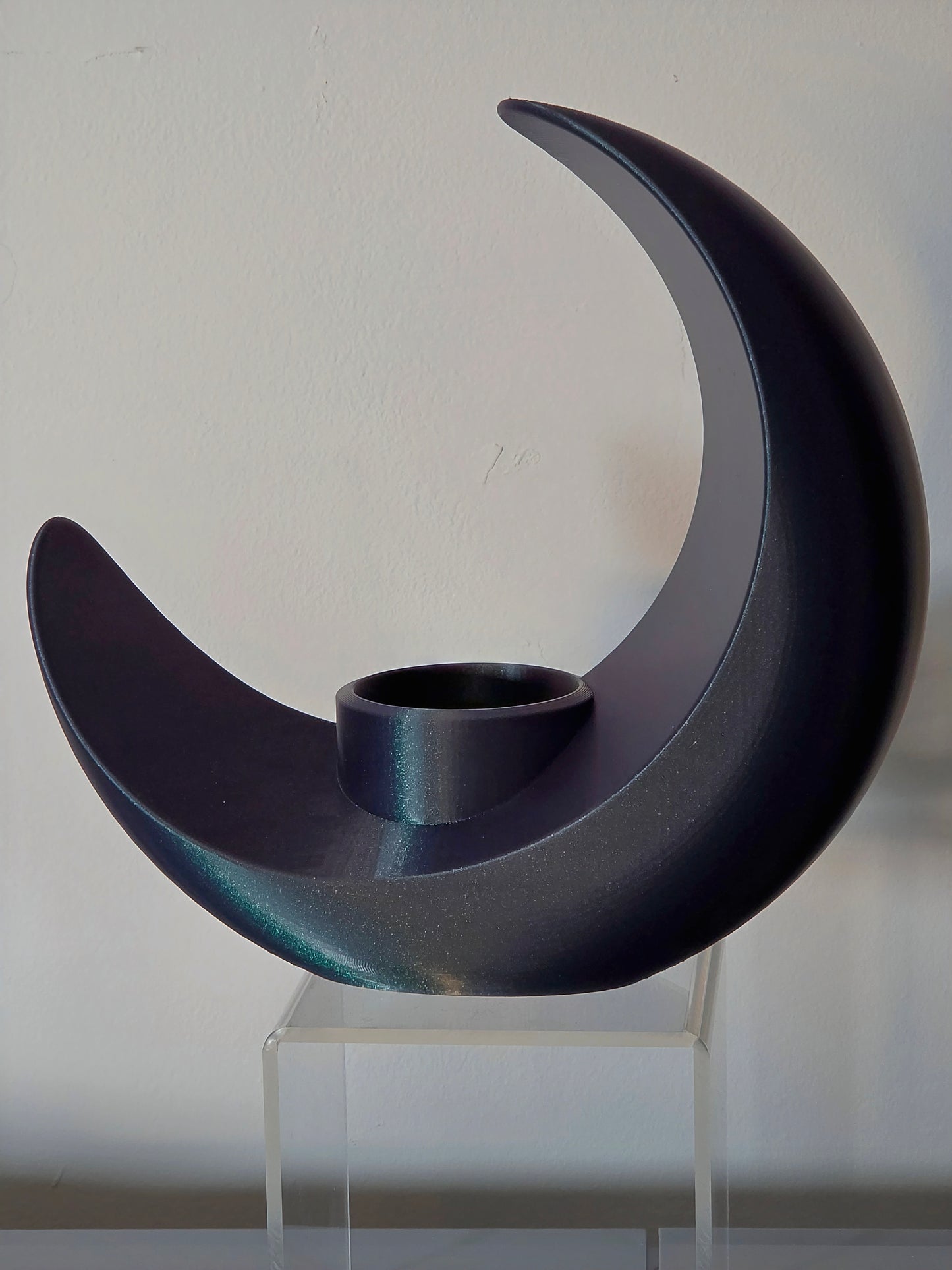 Black crescent moon-shaped candle holder on a clear stand against a white background