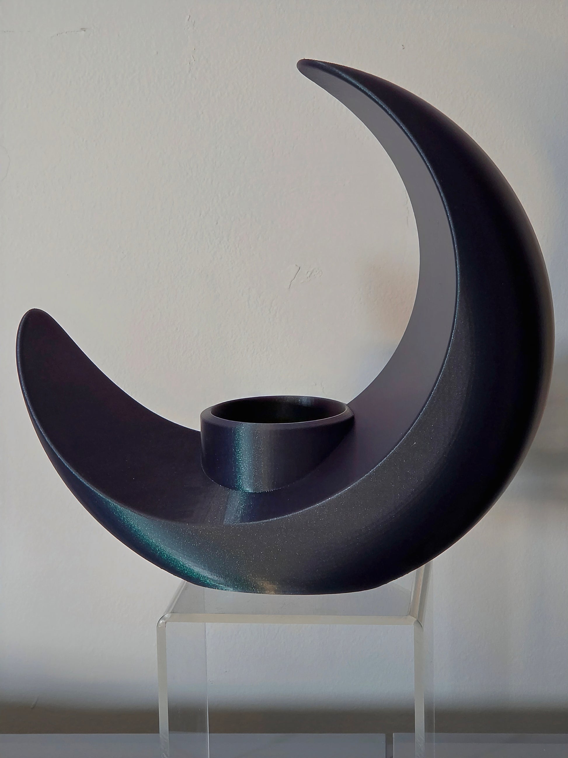 Black crescent moon-shaped candle holder on a clear stand against a white background