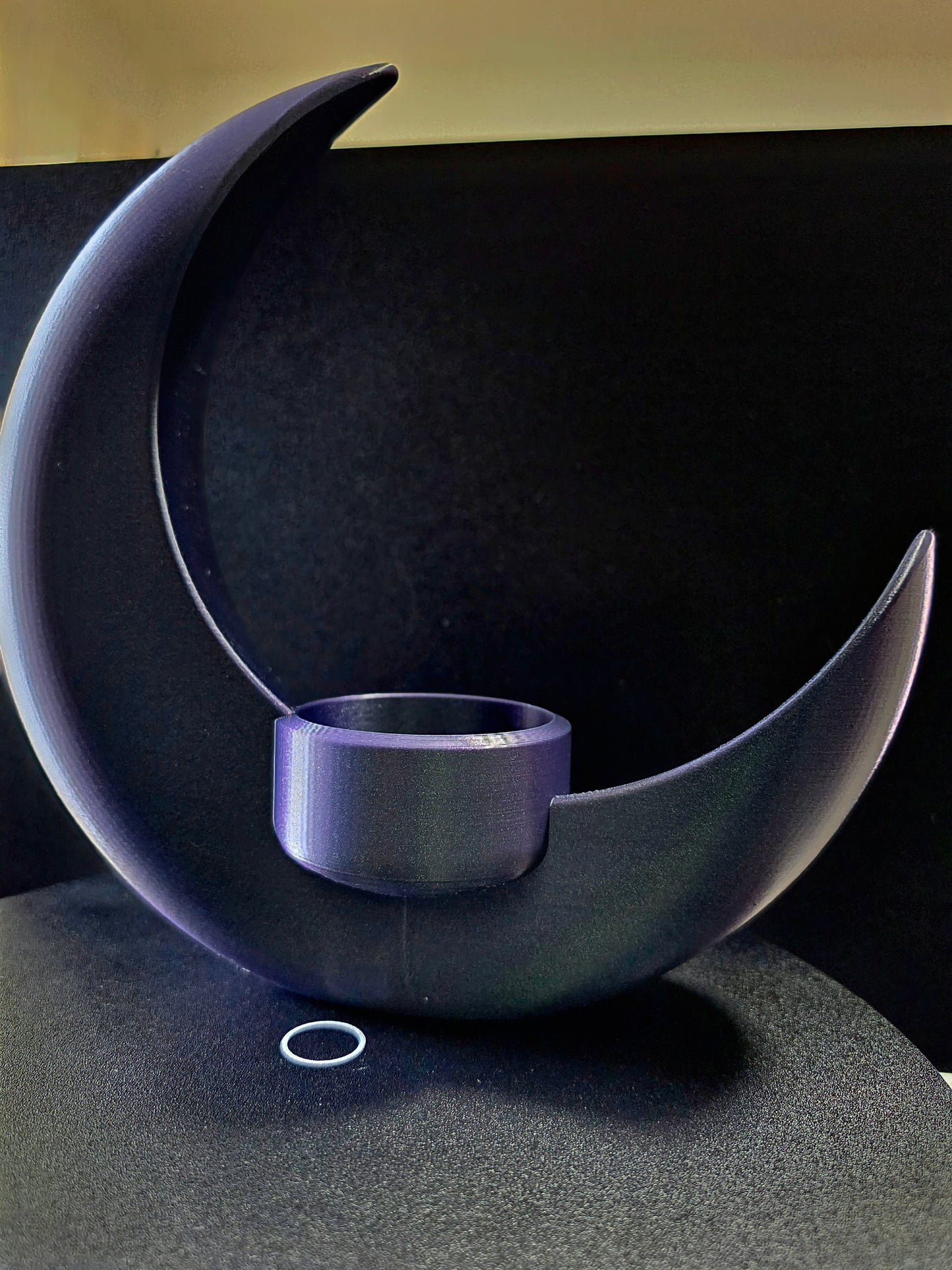 Decorative object shaped like a crescent moon with a small bowl inside on a dark background