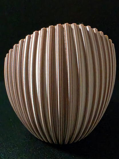 A ribbed, dome-shaped decorative object with a metallic bronze finish, photographed against a solid black background.
