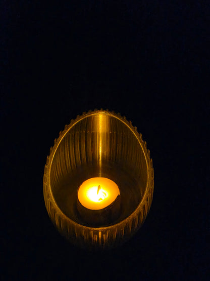 Close-up of a lit candle inside a textured gold holder against a black background