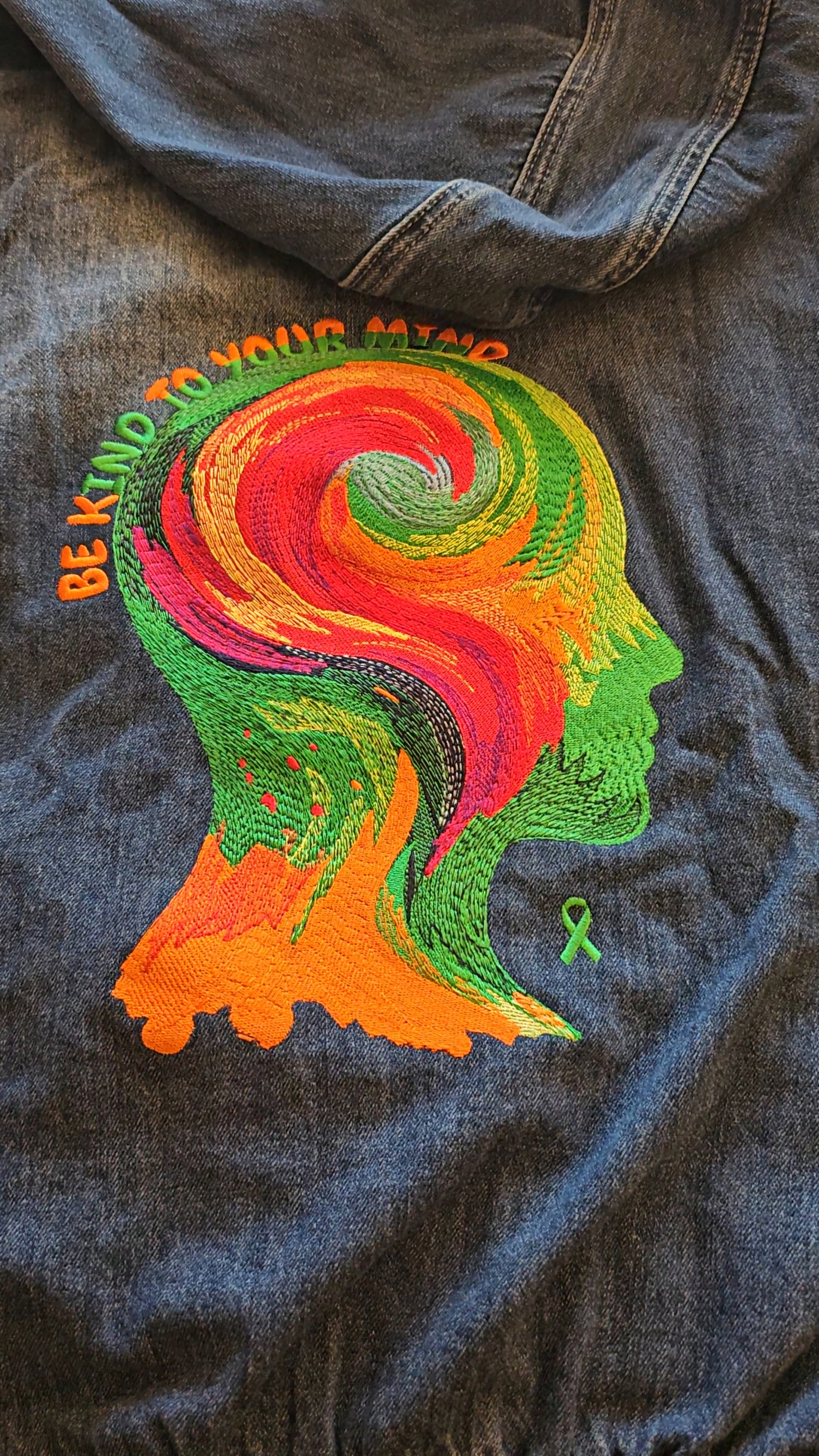 Colorful embroidered design on a denim jacket with 'Be Kind' text.