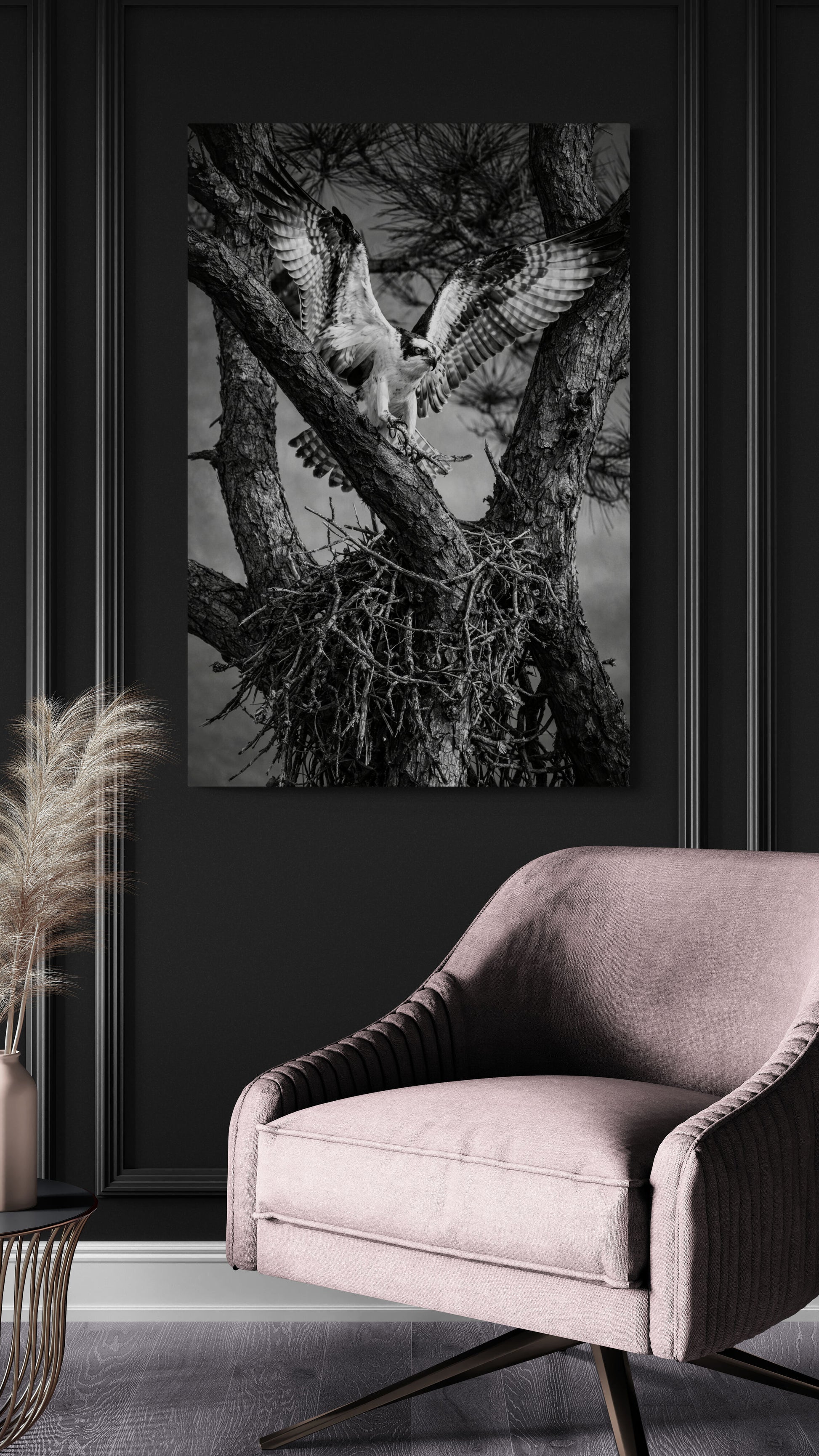 Framed black and white nature print on a dark wall with a pink chair below.