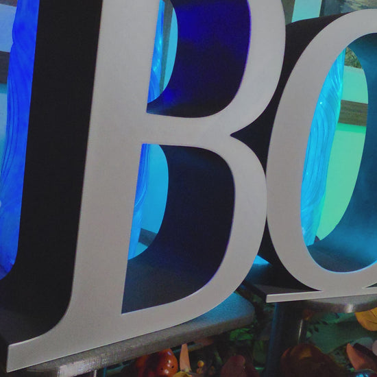 Large 9 inch letters that spell BOO placed on a console with fall decor. The video pans horizontally over each letter that is black with a white front layer.